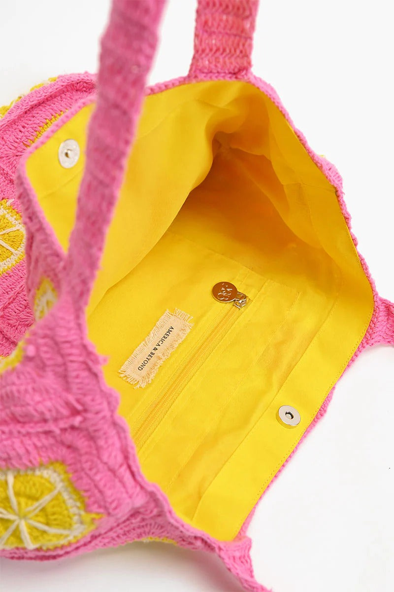 A vibrant pink and yellow crochet beach tote with metallic button closure and double shoulder straps.