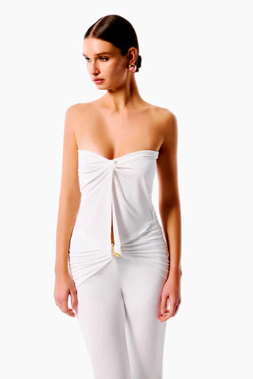 A woman wearing a white strapless top with a twisted detail at the bust, paired with matching white pants.