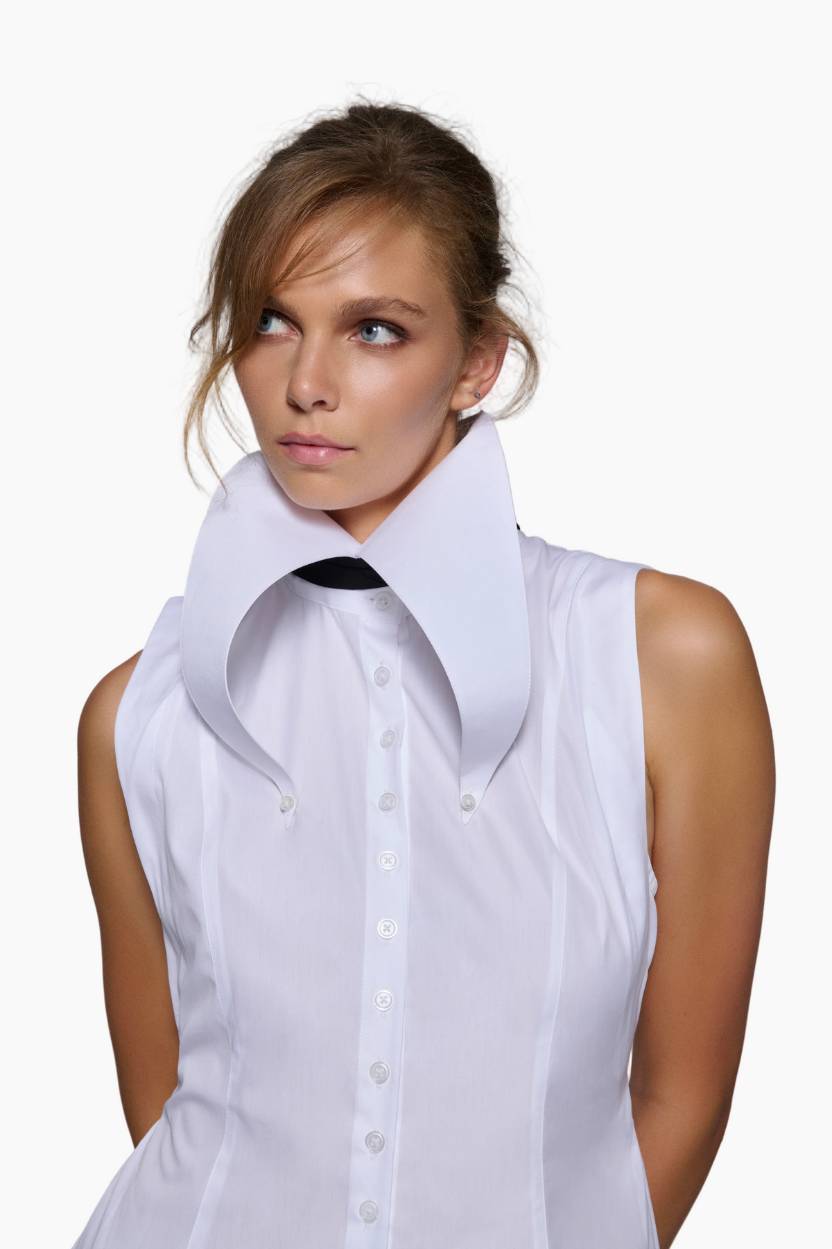 Woman wearing a white sleeveless blouse with a high collar against a gray background