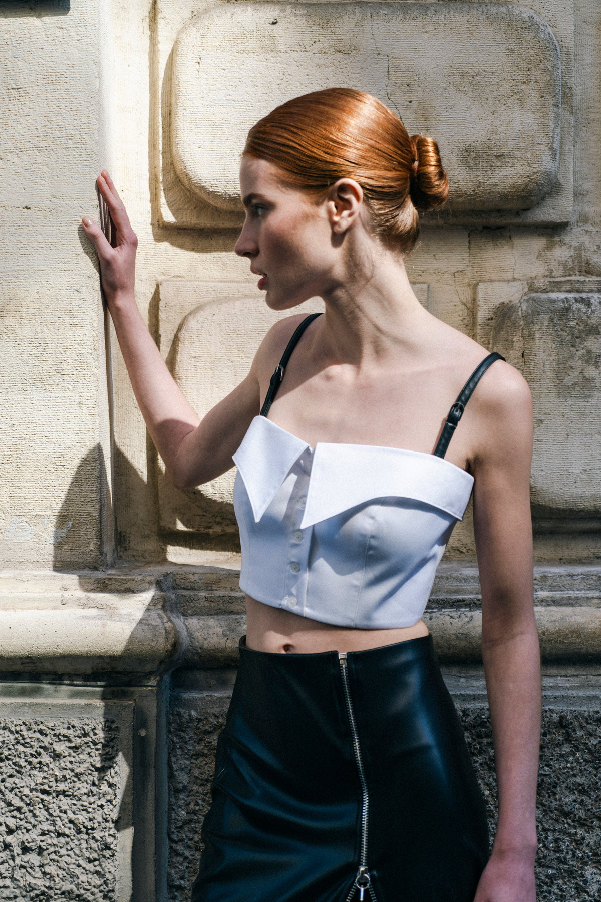 A woman wearing a white gabardine shirt bustier with two black belts as straps and a black skirt.