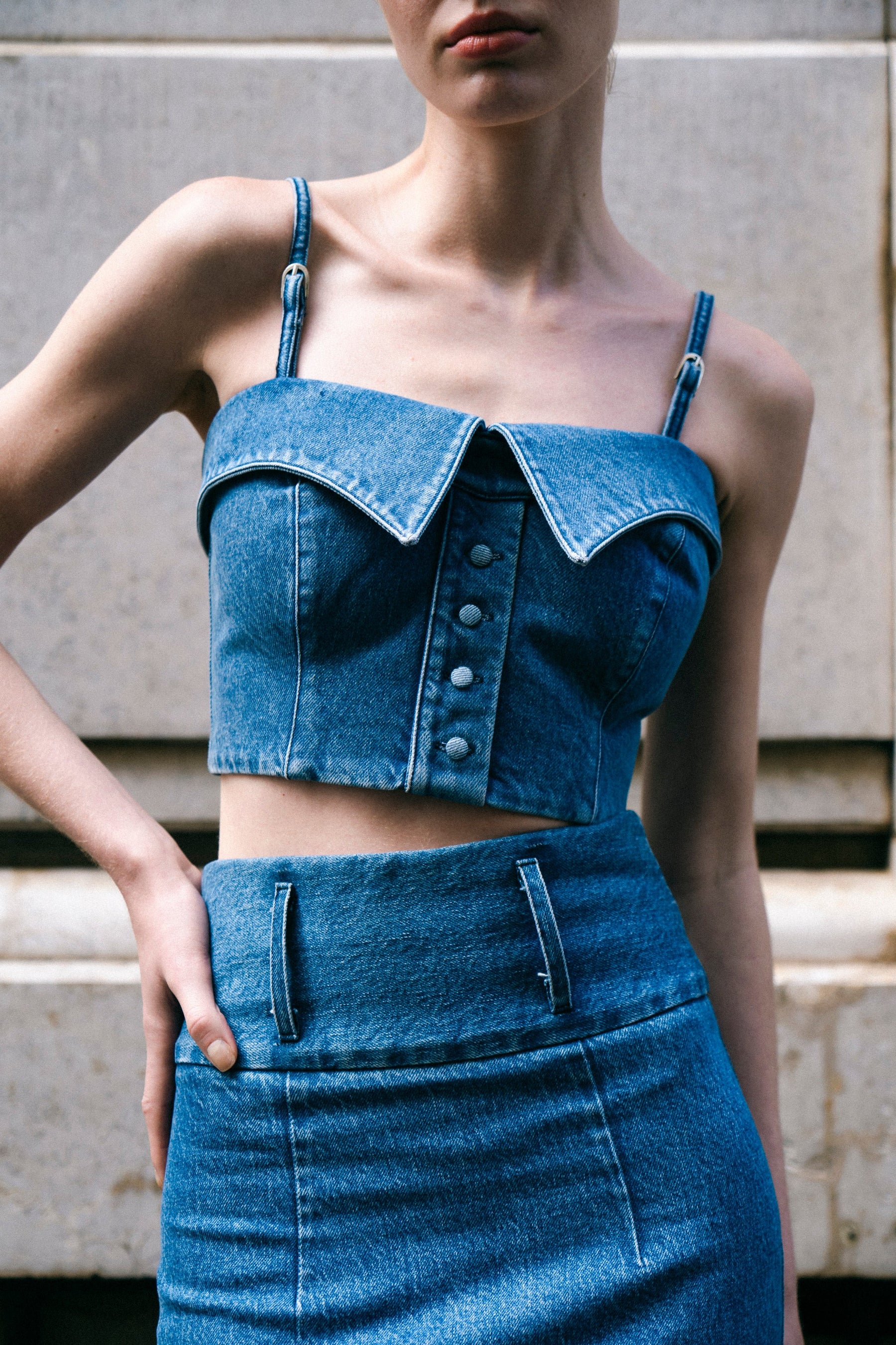 A woman wearing a blue denim shirt bustier with two collar details and shirt placket, paired with sunglasses and a denim skirt.