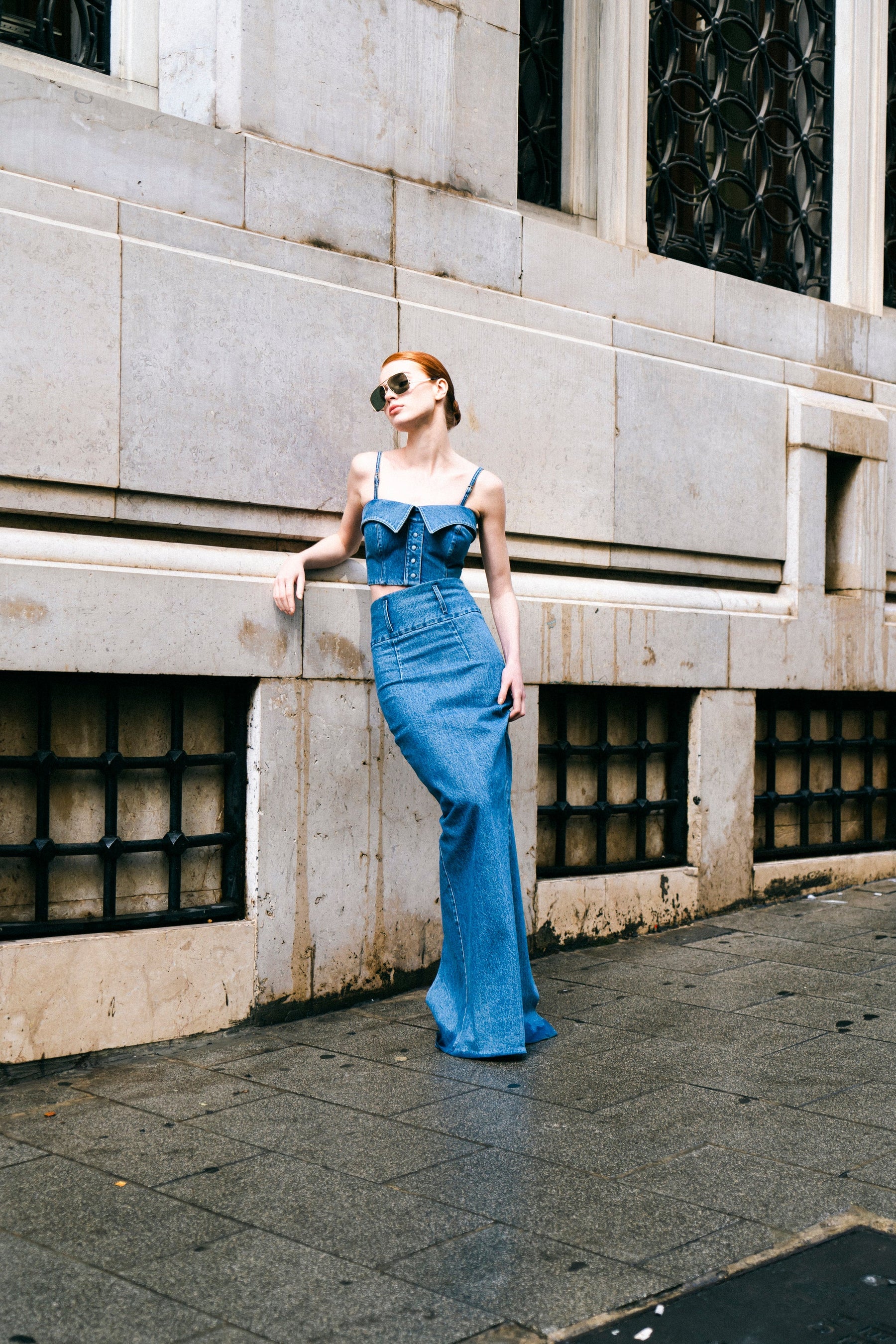 A woman wearing a blue denim shirt bustier with two collar details and shirt placket, paired with sunglasses and a denim skirt.