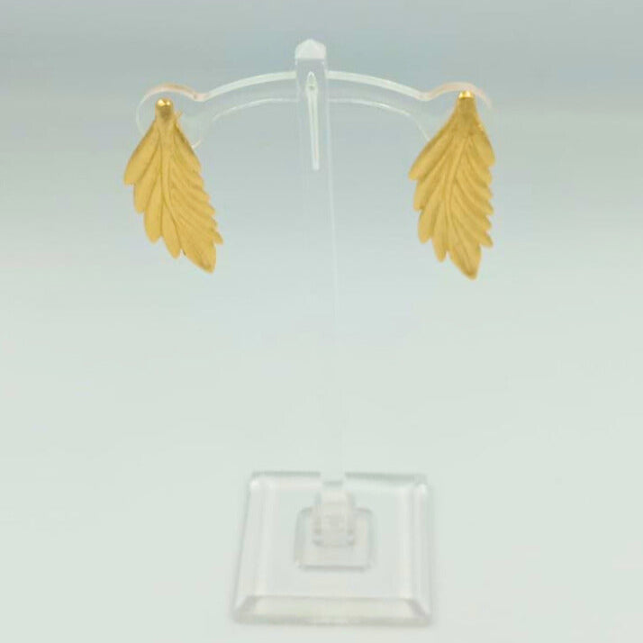 Gold leaf-shaped earrings on a clear stand against a light gray background