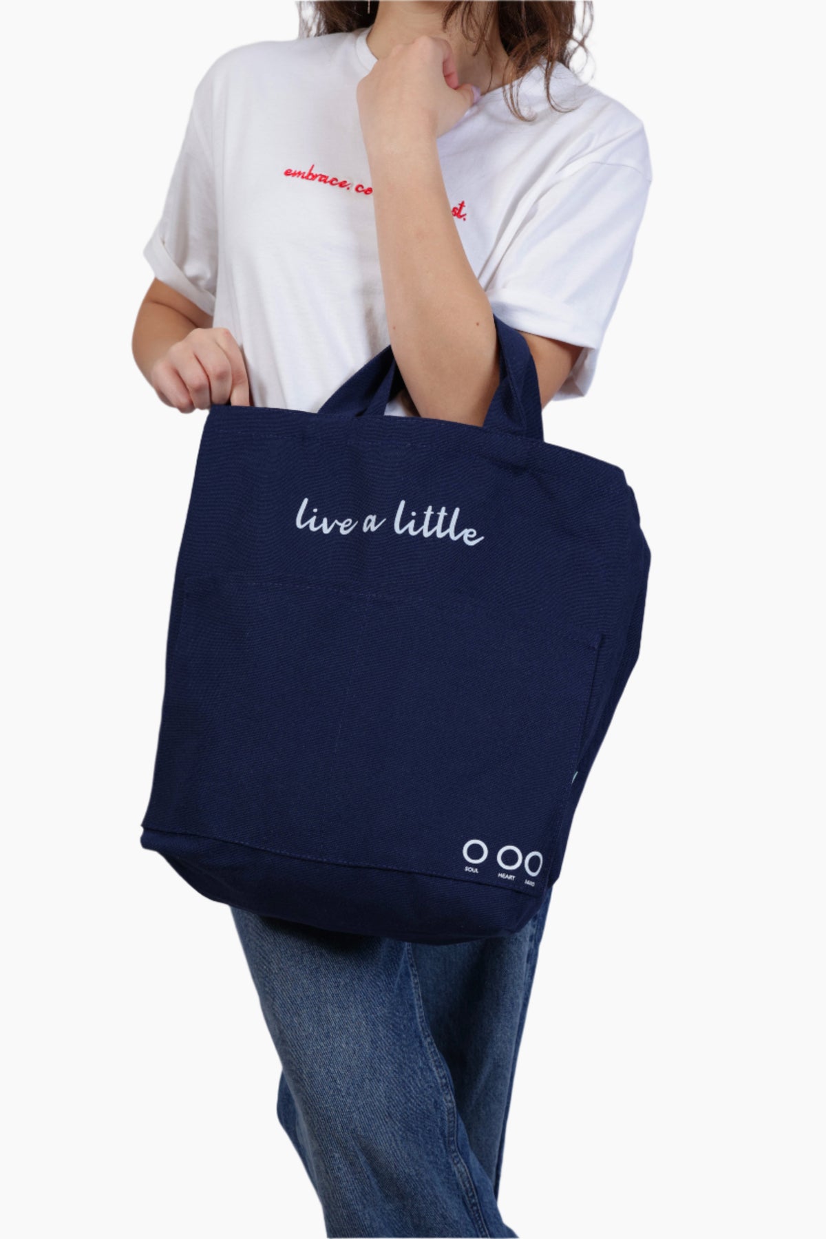 Person holding a navy blue tote bag with 'live a little' text