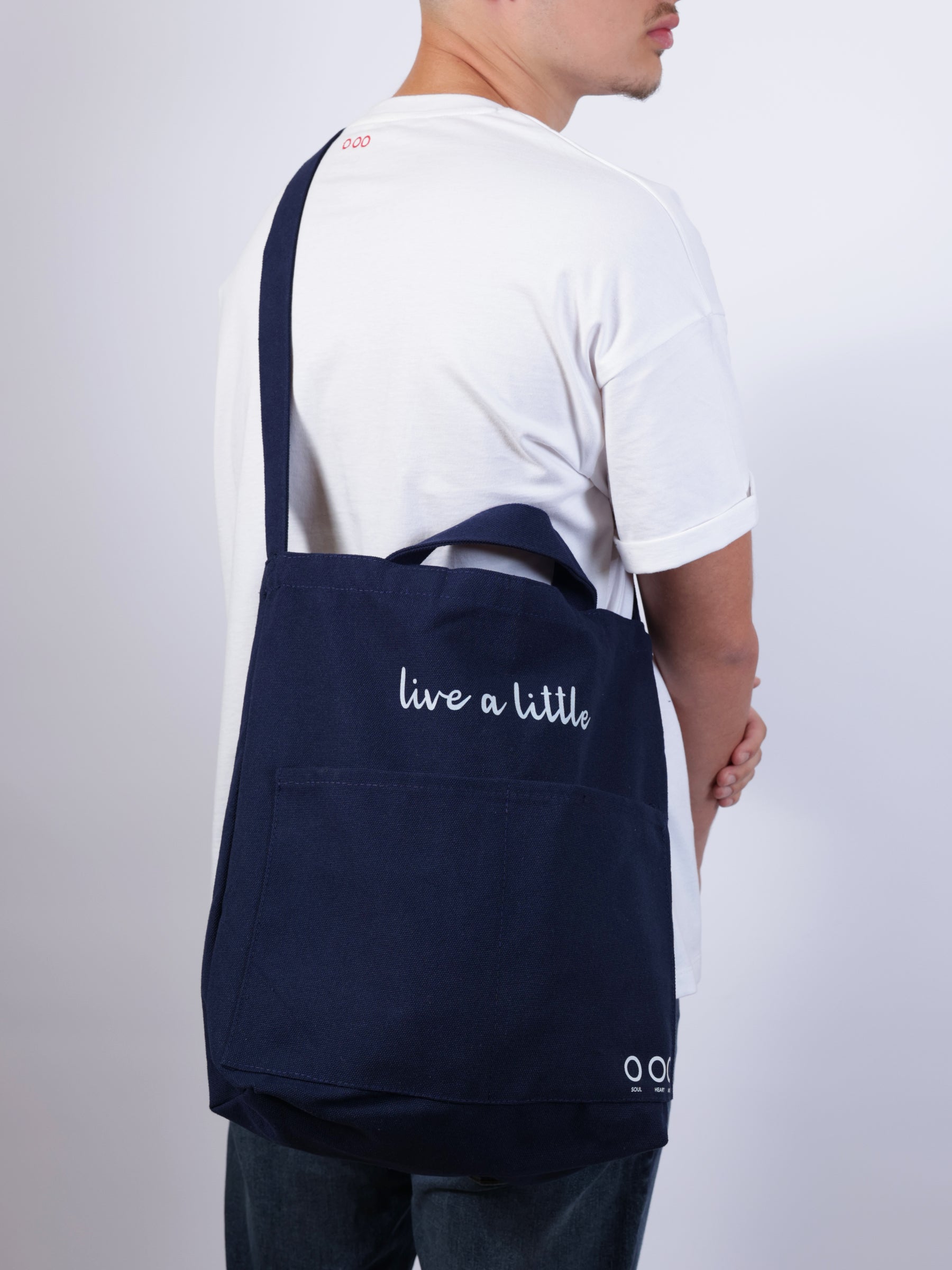 Person holding a navy blue tote bag with 'live a little' text