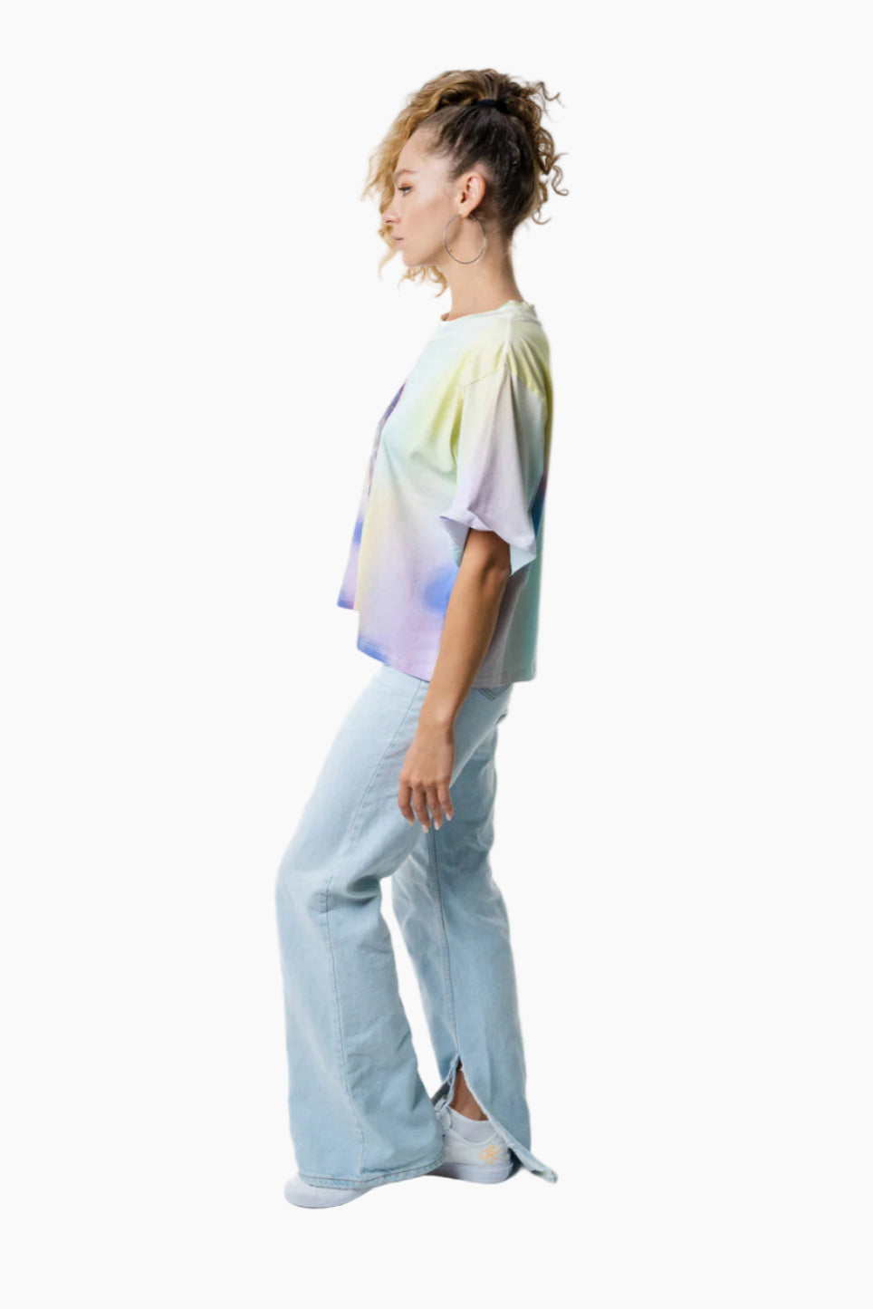 Person wearing a tie-dye shirt and light blue jeans on a white background