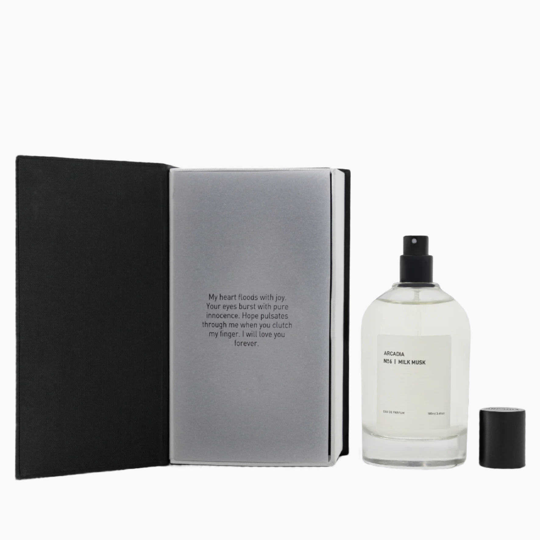 Perfume bottle with black cap and white label next to an open book . Vanilla, musk, cashmere wood, sandalwood and amber.