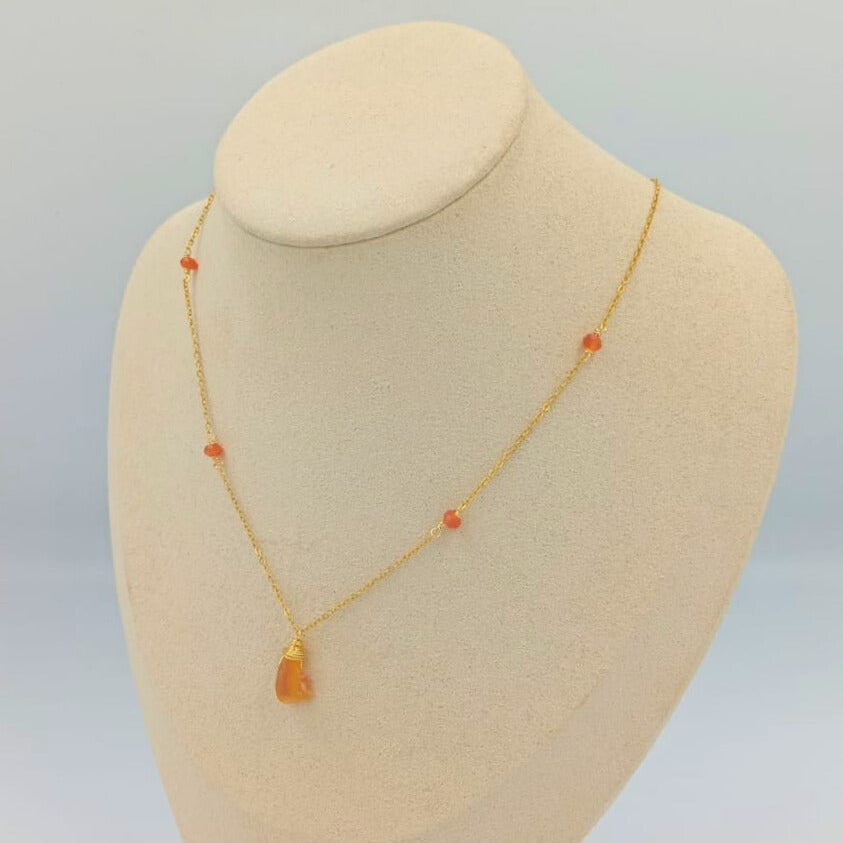 Gold necklace with orange beads on a mannequin bust against a light gray background