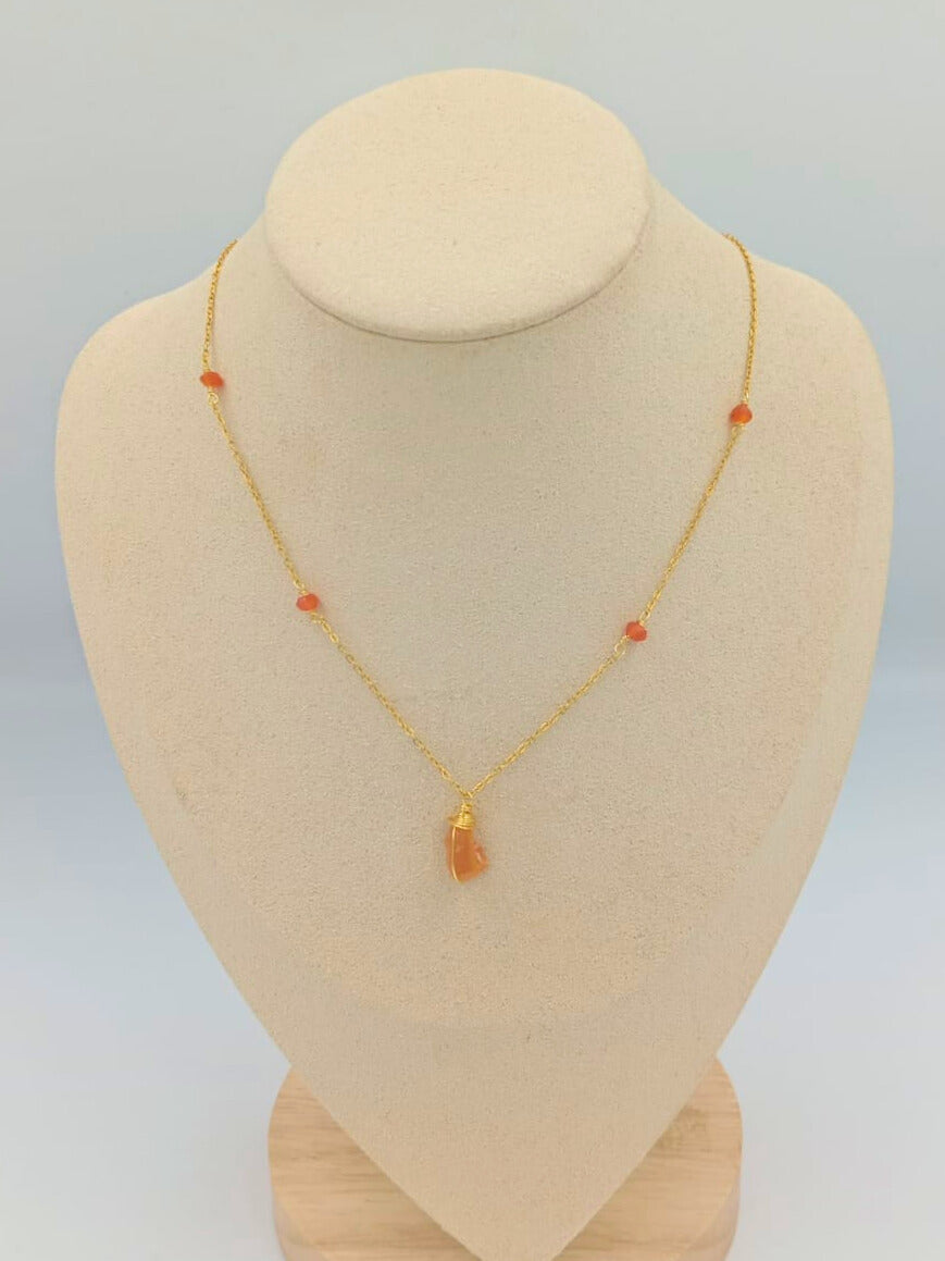 Gold necklace with orange beads on a mannequin bust against a light gray background