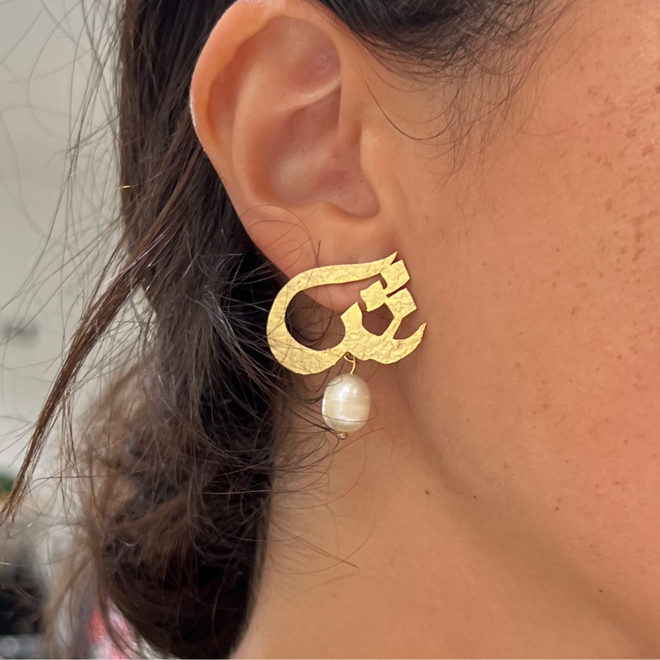 Gold earrings with a pearl drop worn by a person