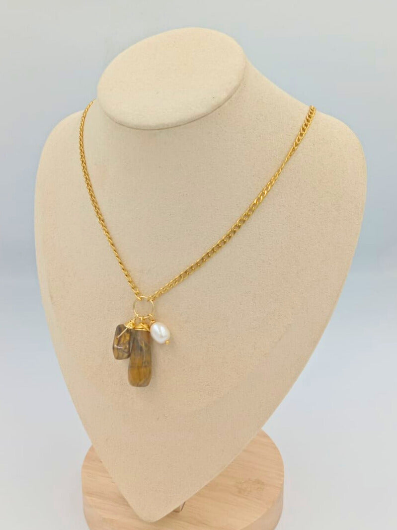 A gold-colored necklace with a chain link design, featuring three precious stones pendants displayed on a mannequin bust.