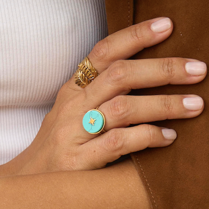 Hand wearing a turquoise ring with gold accents on a brown surface
