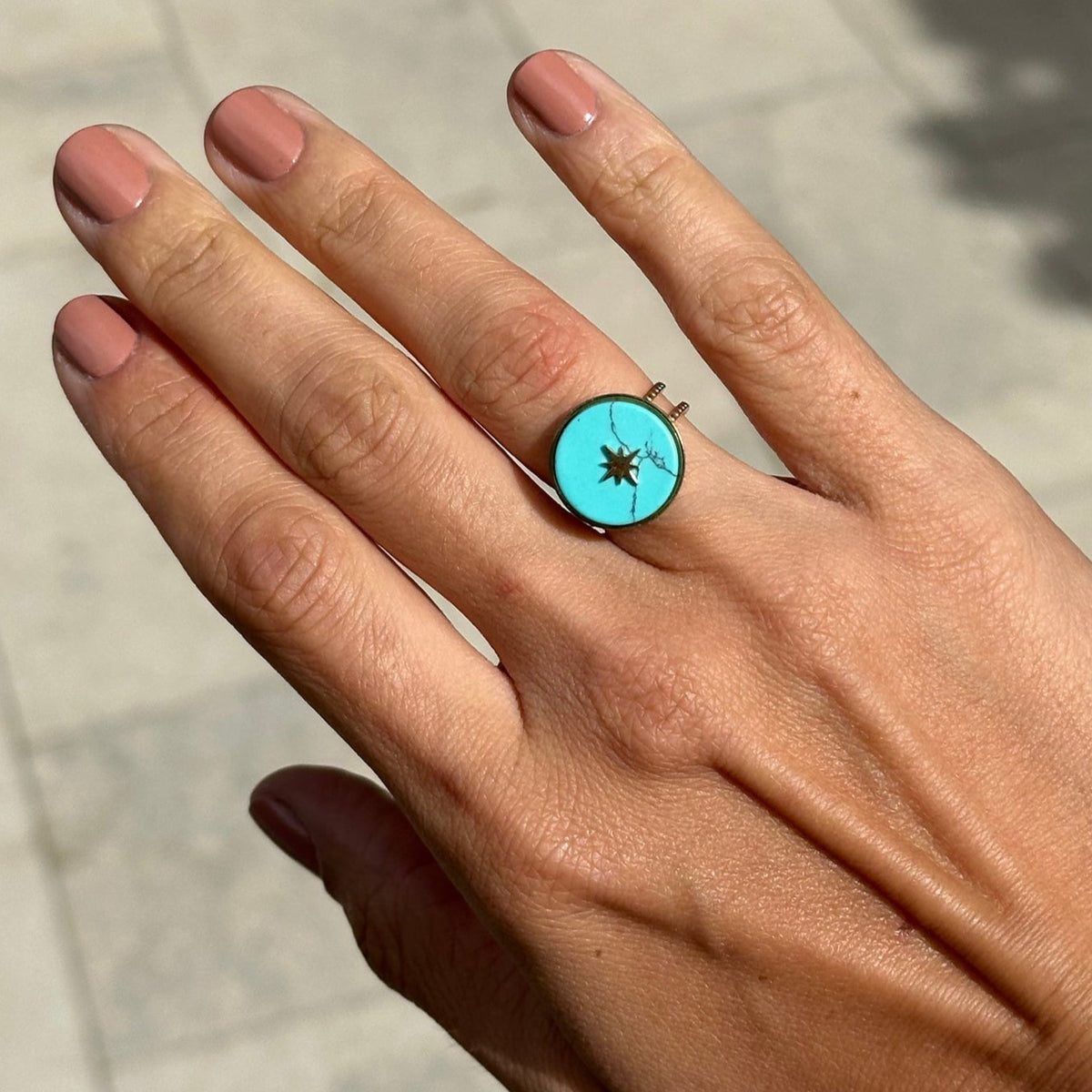 Hand wearing a turquoise ring with a star design on a pavement background