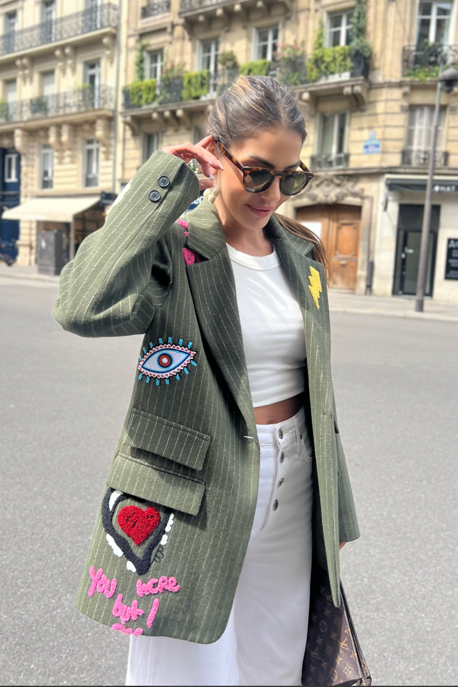 Woman wearing a green blazer with colorful designs on a city street.