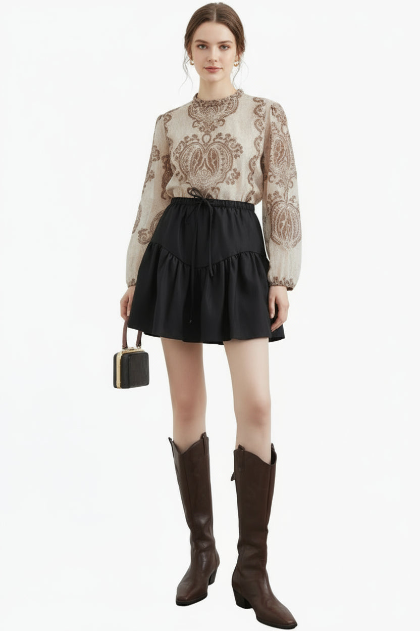 Woman wearing a patterned blouse, black skirt, and brown knee-high boots