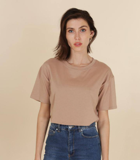 Woman wearing a beige t-shirt and blue jeans against a beige background