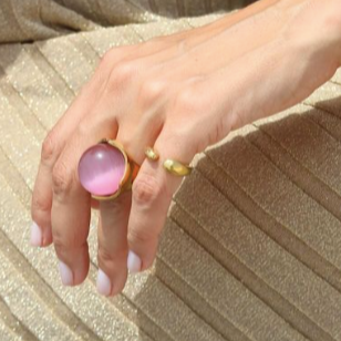 Hand wearing a pink ring with a gold band on a beige fabric background