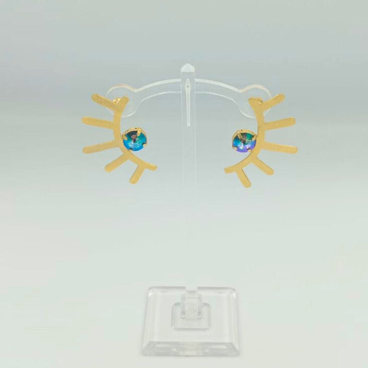 Gold earrings with blue gemstones on a clear stand against a light gray background