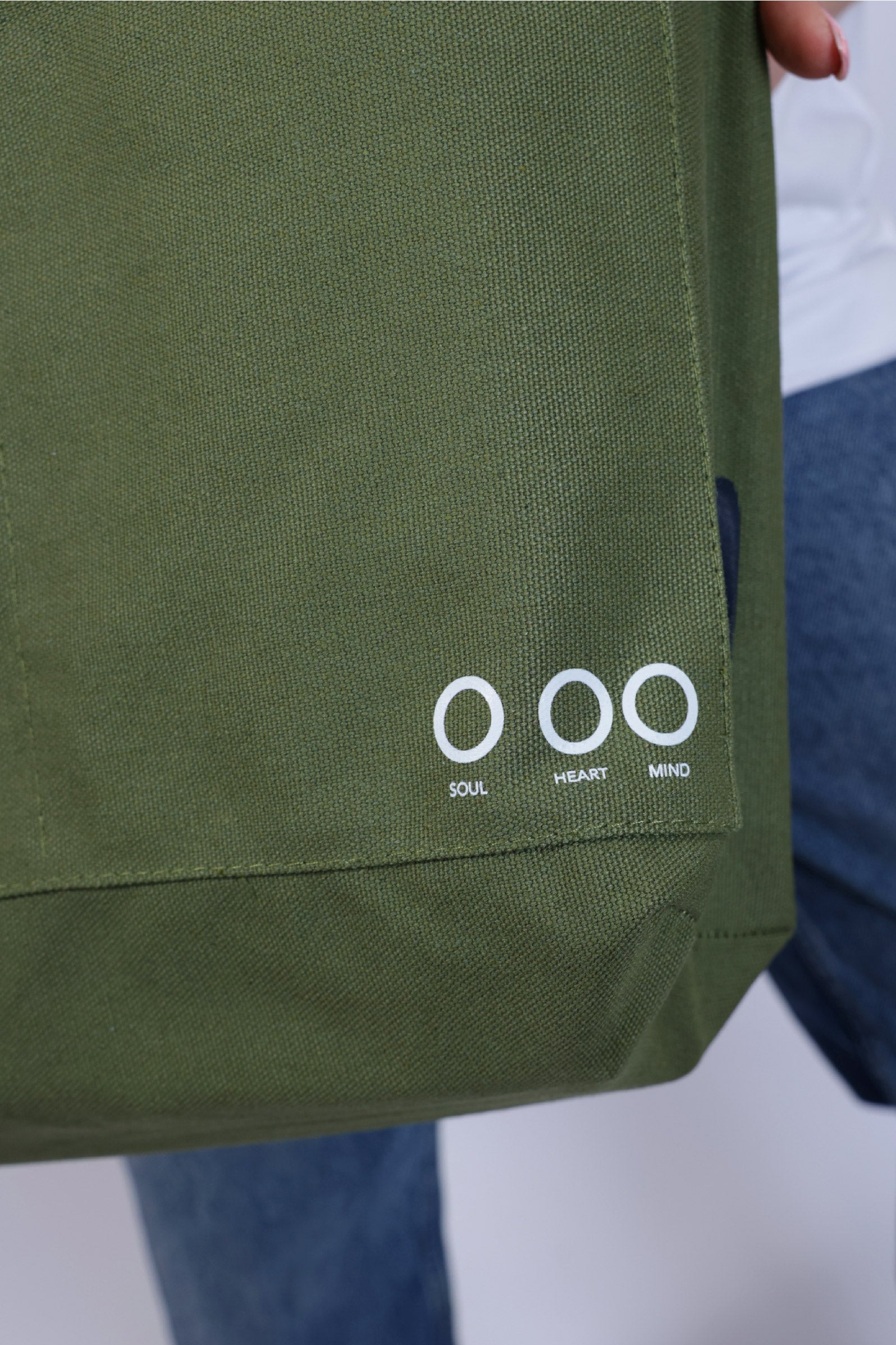 Green bag with 'Soul Heart Mind' text held by a person wearing blue jeans