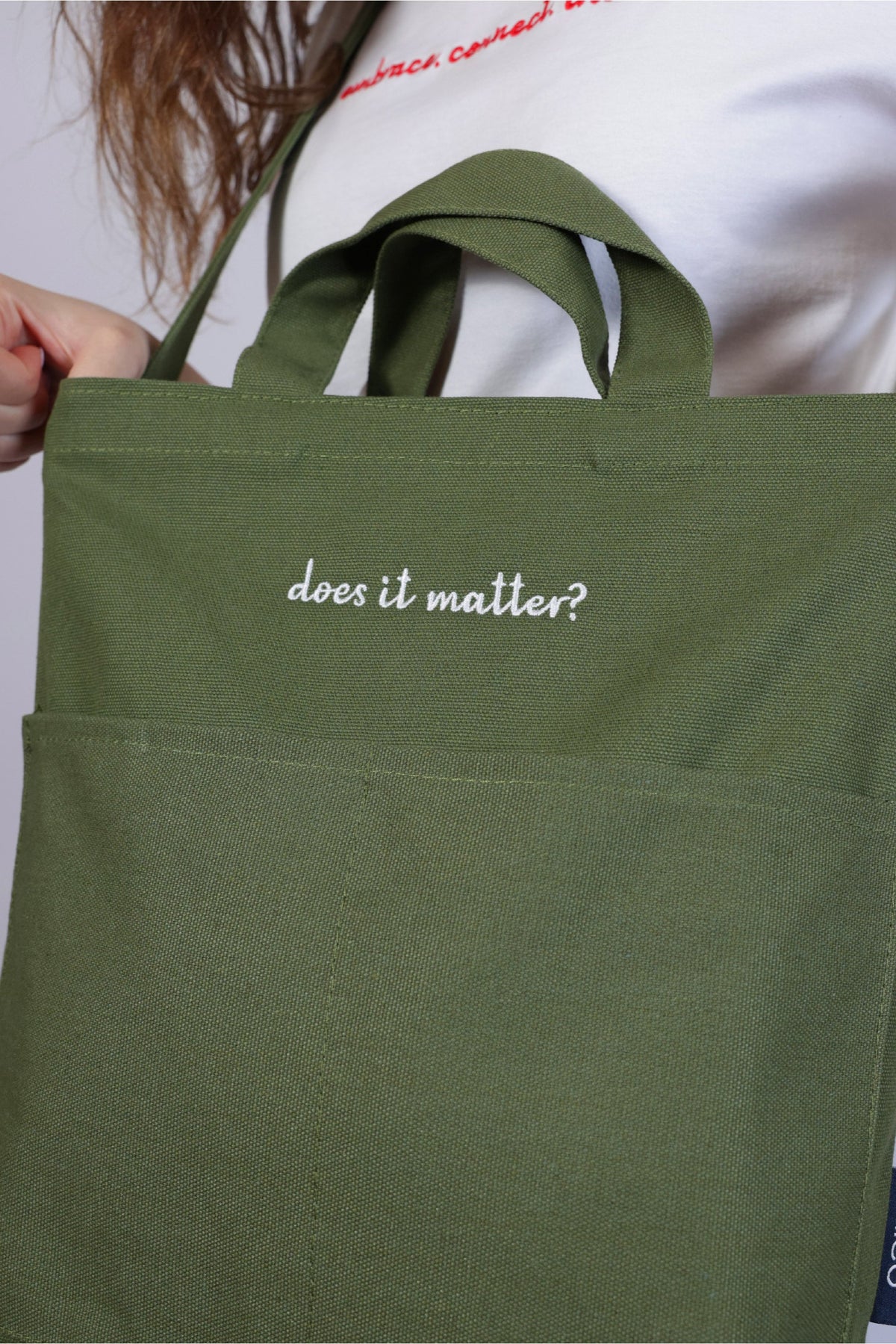 Green tote bag with 'does it matter?' text held by a person