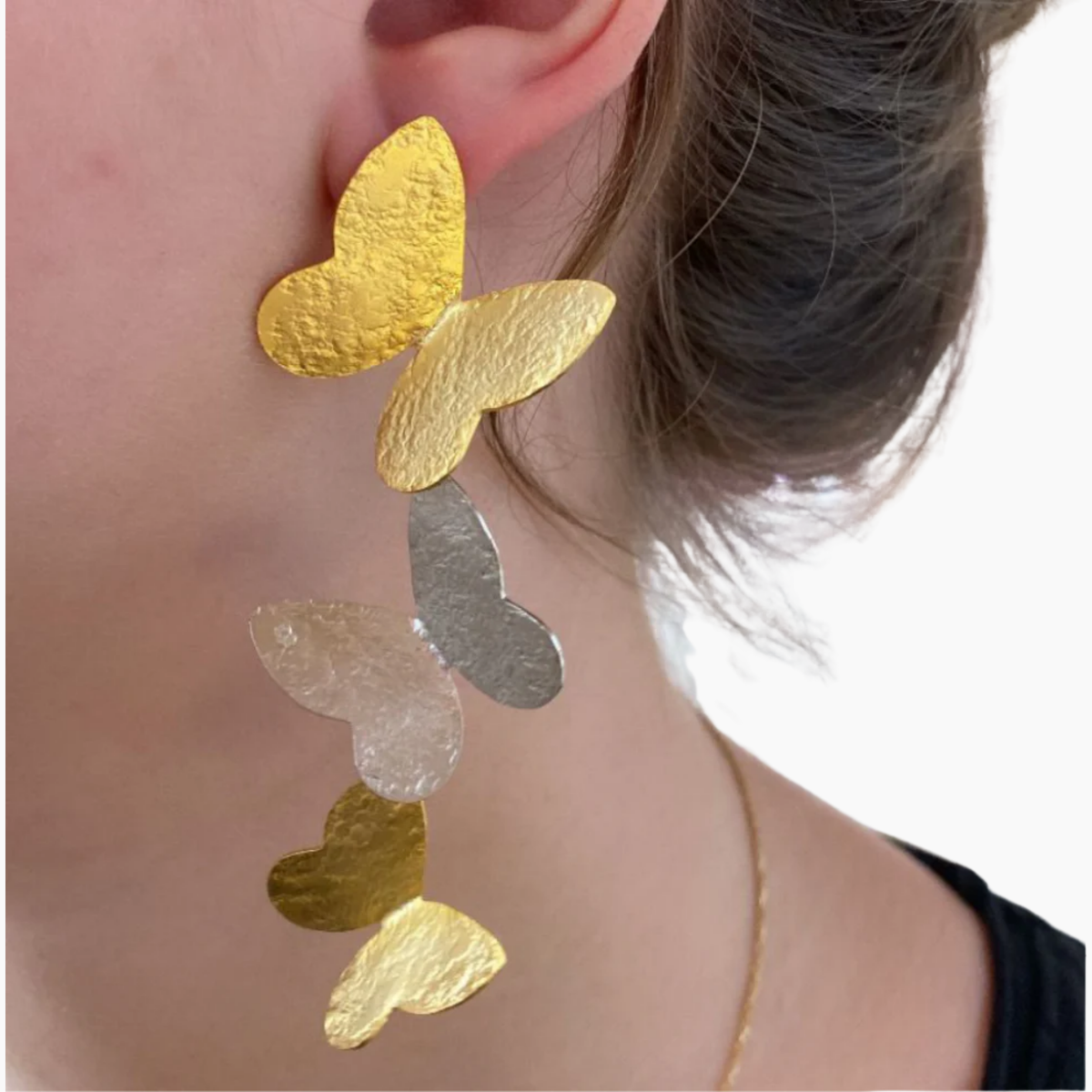 Gold and silver heart-shaped earrings worn by a person.