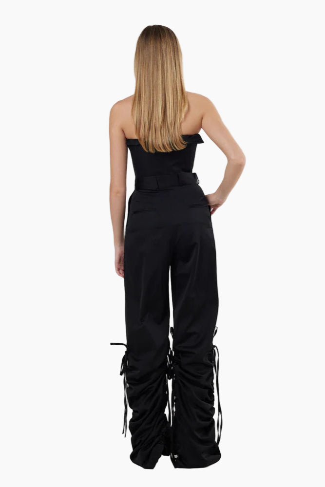 Woman wearing a black strapless top with a pant with ruched sides on a white background