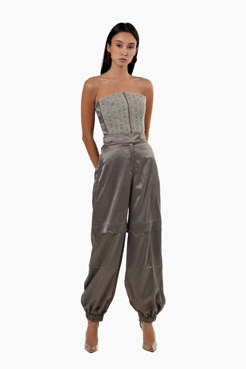Woman wearing a strapless jumpsuit with a textured top and shiny pants on a white background