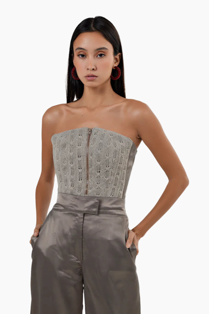 Woman wearing a strapless top with lace detailing and high-waisted pants on a white background
