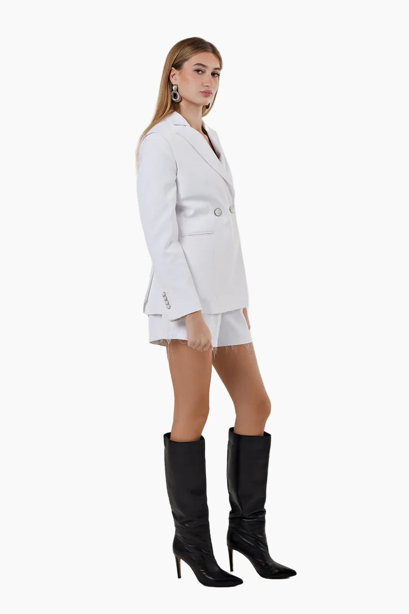Woman wearing a white suit with black knee-high boots on a white background