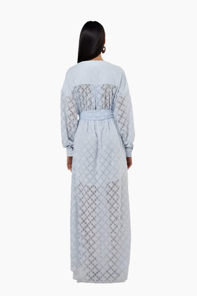 Woman wearing a light blue patterned dress with a slit. Flared floor-length dress with a V-neckline, balloon sleeves, two side slits, and a waist belt.