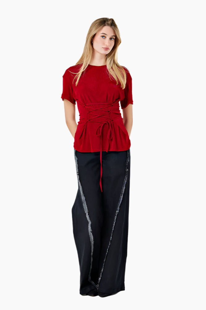 Woman wearing a red top and black pants. Oversized T-shirt with side loops and an adjustable waist corset-like belt.