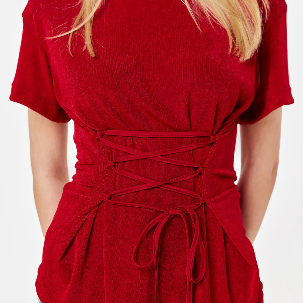 Woman wearing a red top and black pants. Oversized T-shirt with side loops and an adjustable waist corset-like belt.