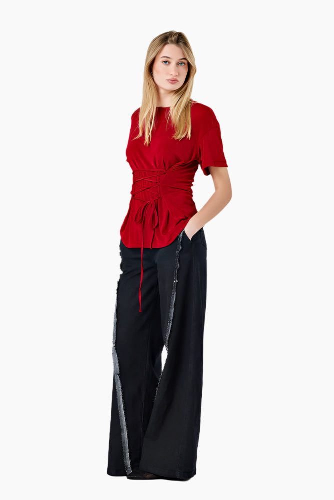 Woman wearing a red top and black pants. Oversized T-shirt with side loops and an adjustable waist corset-like belt.
