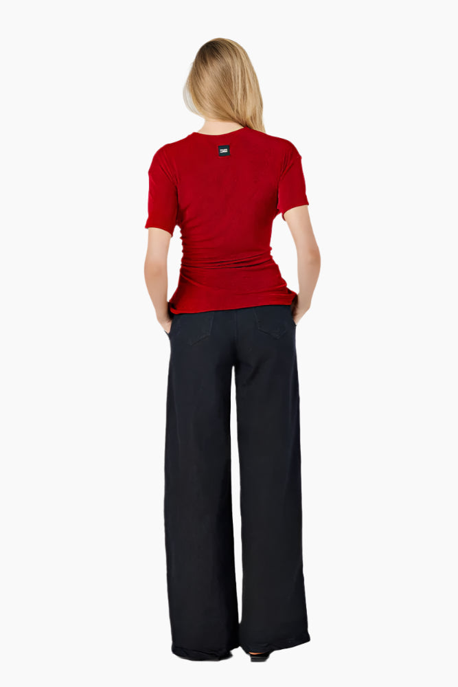 Woman wearing a red top and black pants. Oversized T-shirt with side loops and an adjustable waist corset-like belt.