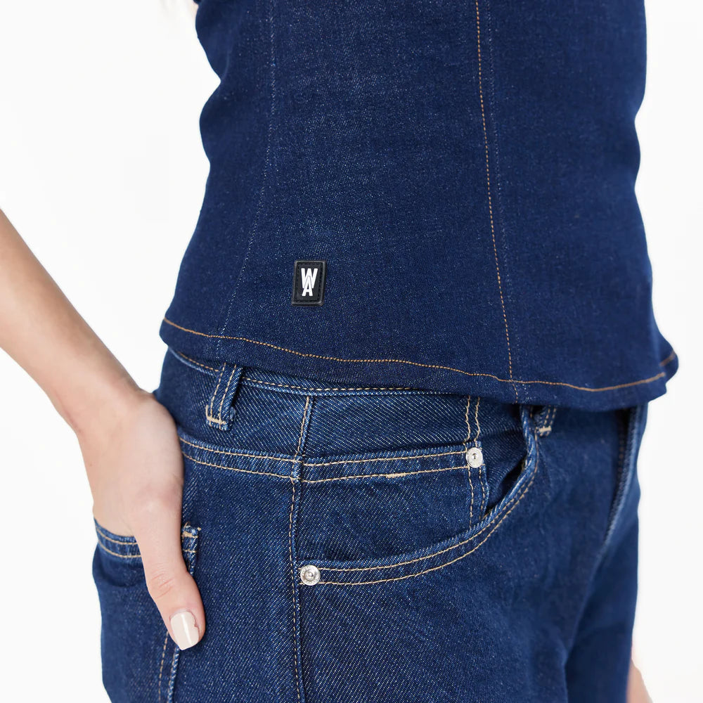 Close-up of a person wearing blue jeans . Fitted top with piping details, corset-like cuts, and topstitching details.