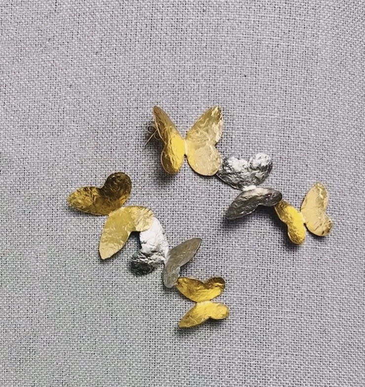 A collection of gold-colored butterfly-shaped earrings displayed on a textured grey surface.