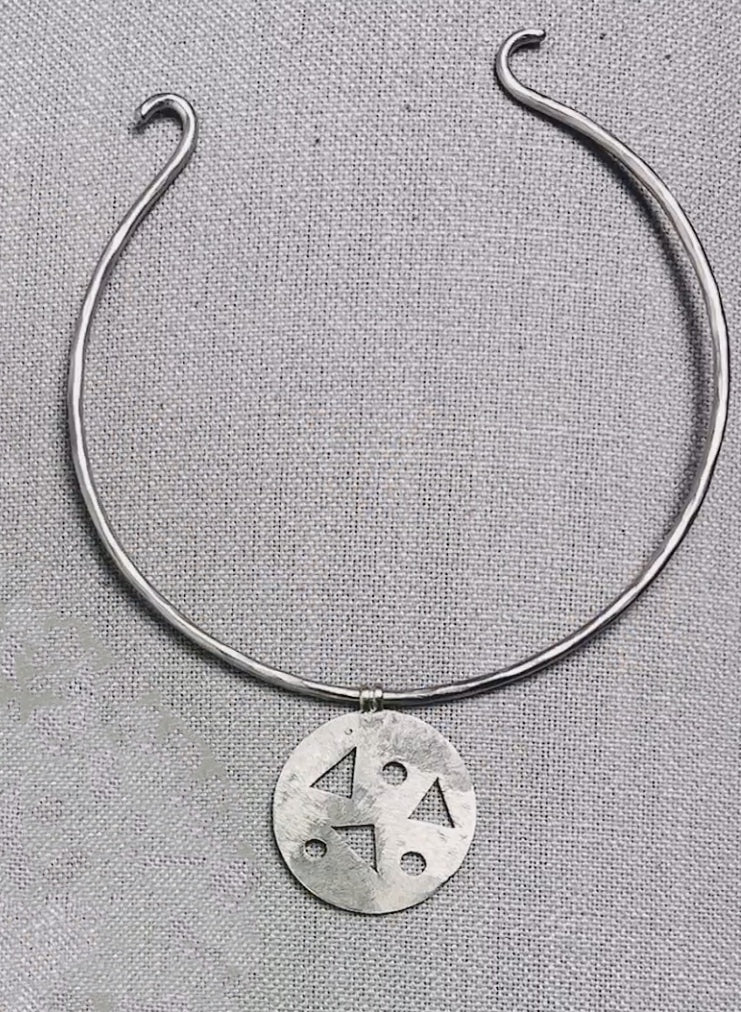 A silver-colored geometric arm necklace displayed on a textured background.