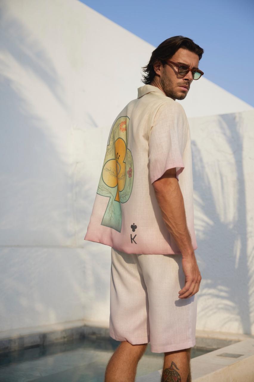 A man standing poolside wearing a white shirt with a key design, white shorts.