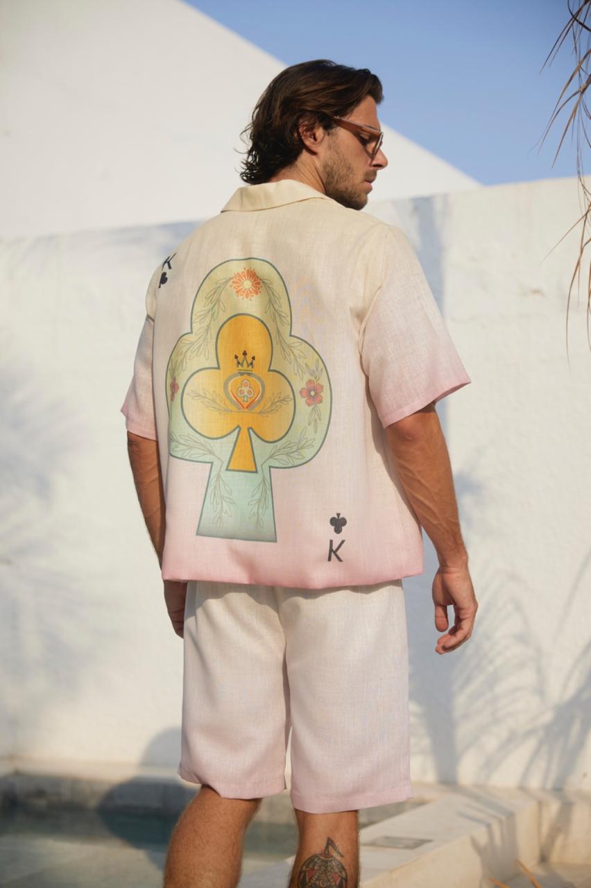 A man wearing a white shirt with a colorful abstract design and white shorts standing in front of a white wall.