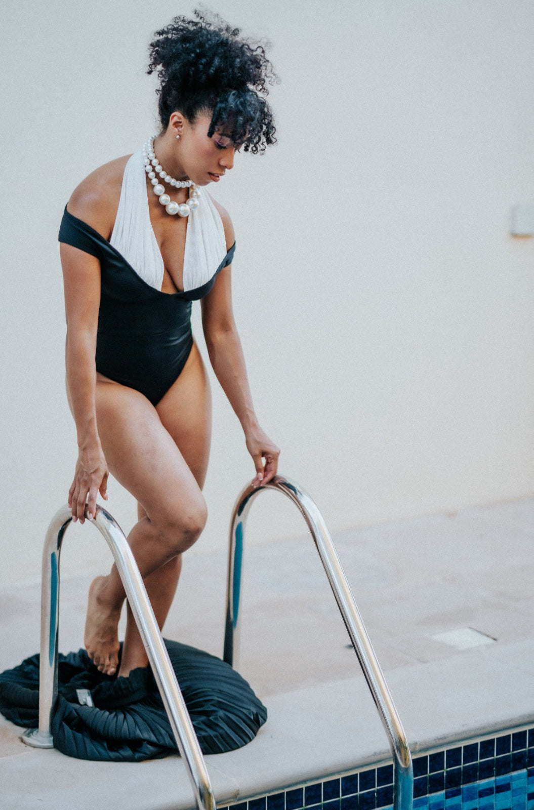 Woman in a black swimsuit with white accents standing on a pool ladder.