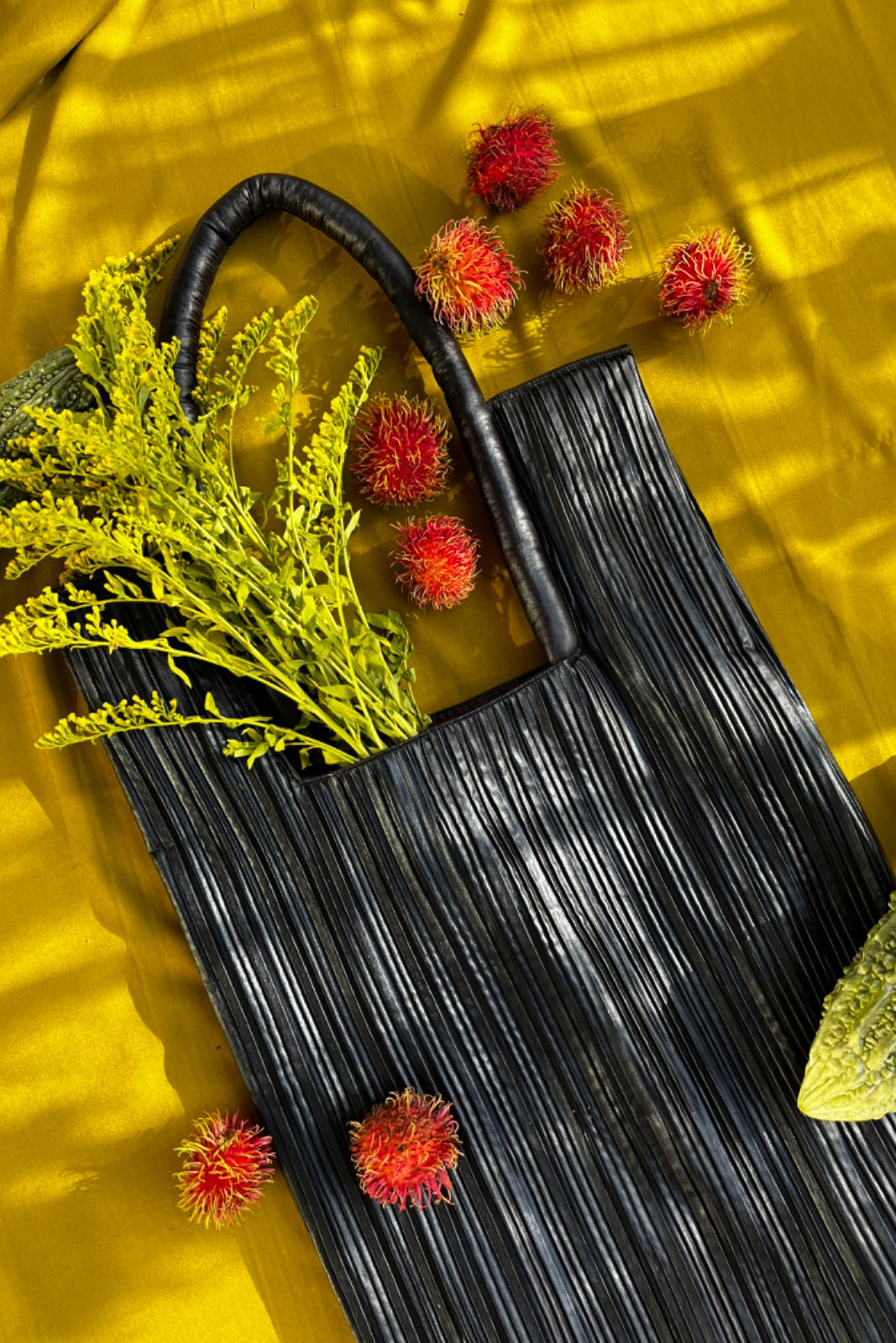 Black woven bag with greenery and red flowers on a yellow background