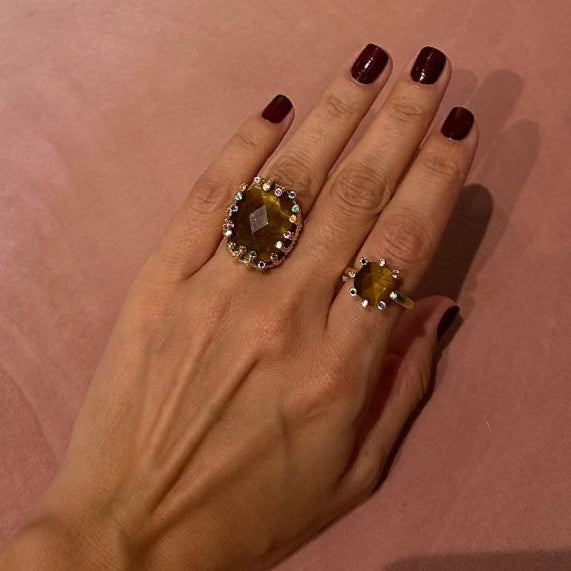 Hand wearing two rings with gemstones on a pink background