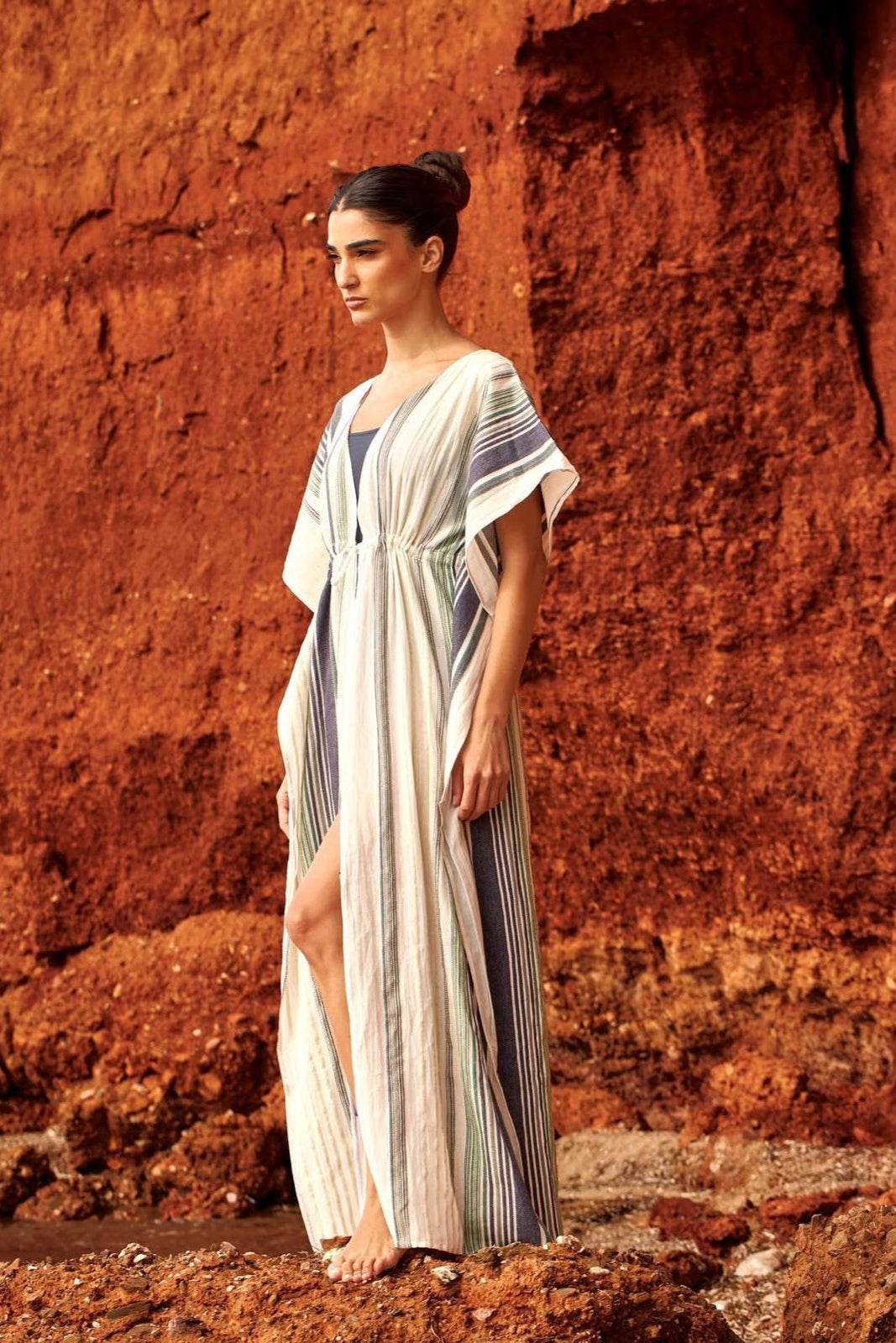 Woman in a long, light-colored dress standing against a red rock wall.
