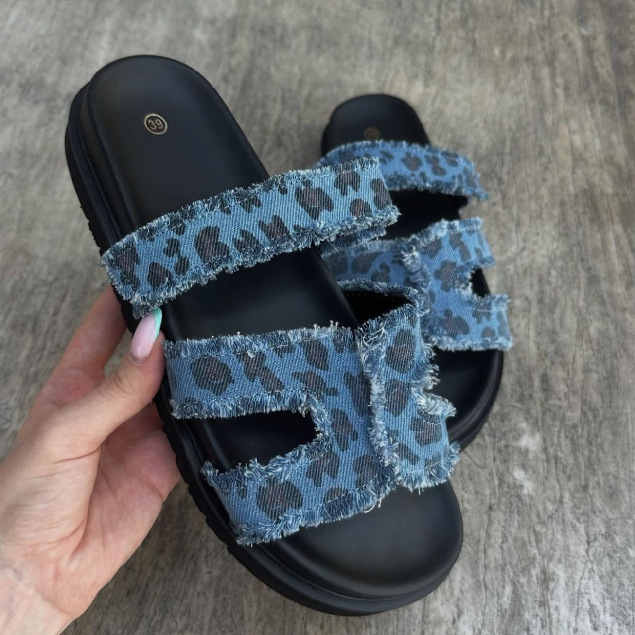 Black sandal with blue leopard print straps held by a hand
