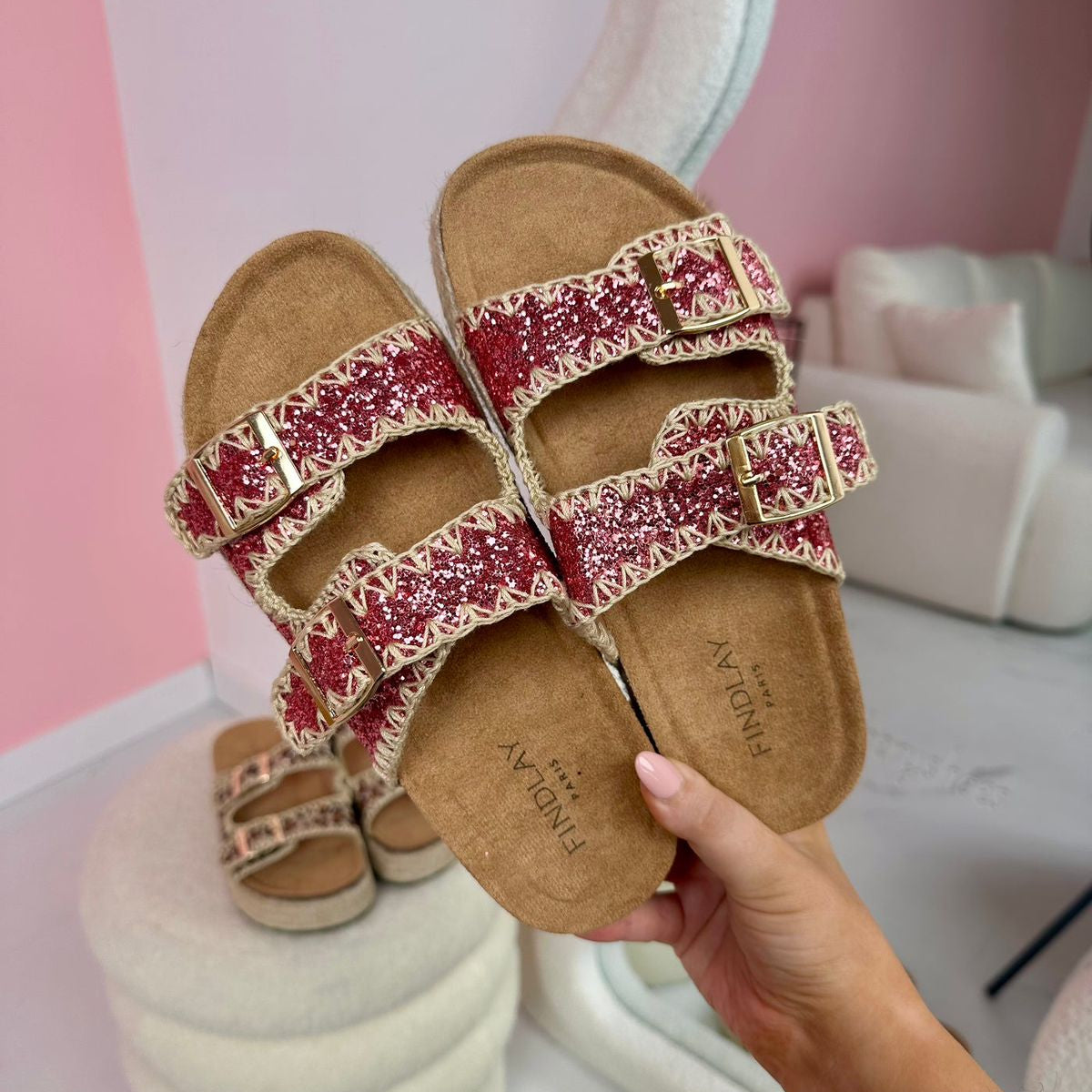 Brown sandals with red glittery straps held by a hand