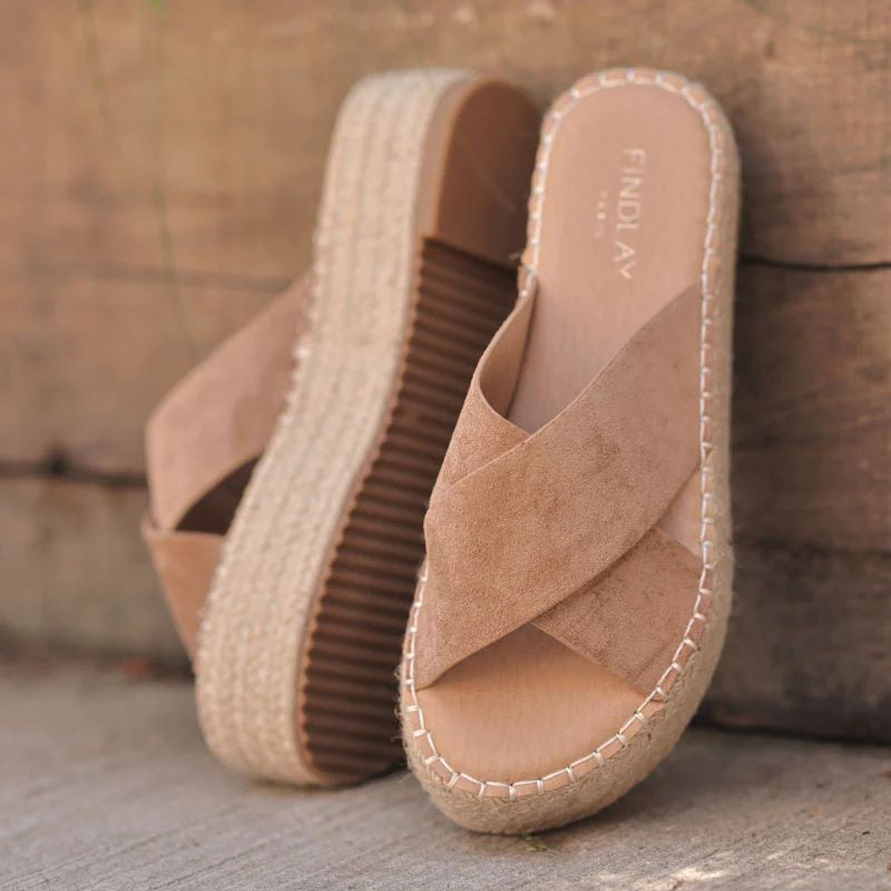 Pair of tan espadrille sandals with woven sole on a stone surface.
