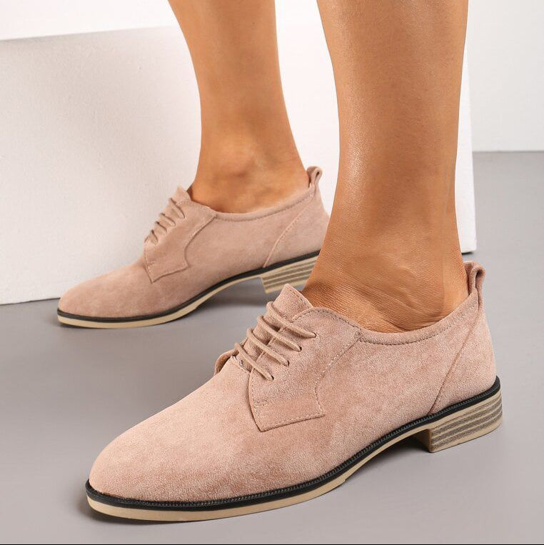 Beige suede shoes worn by a person on a neutral background