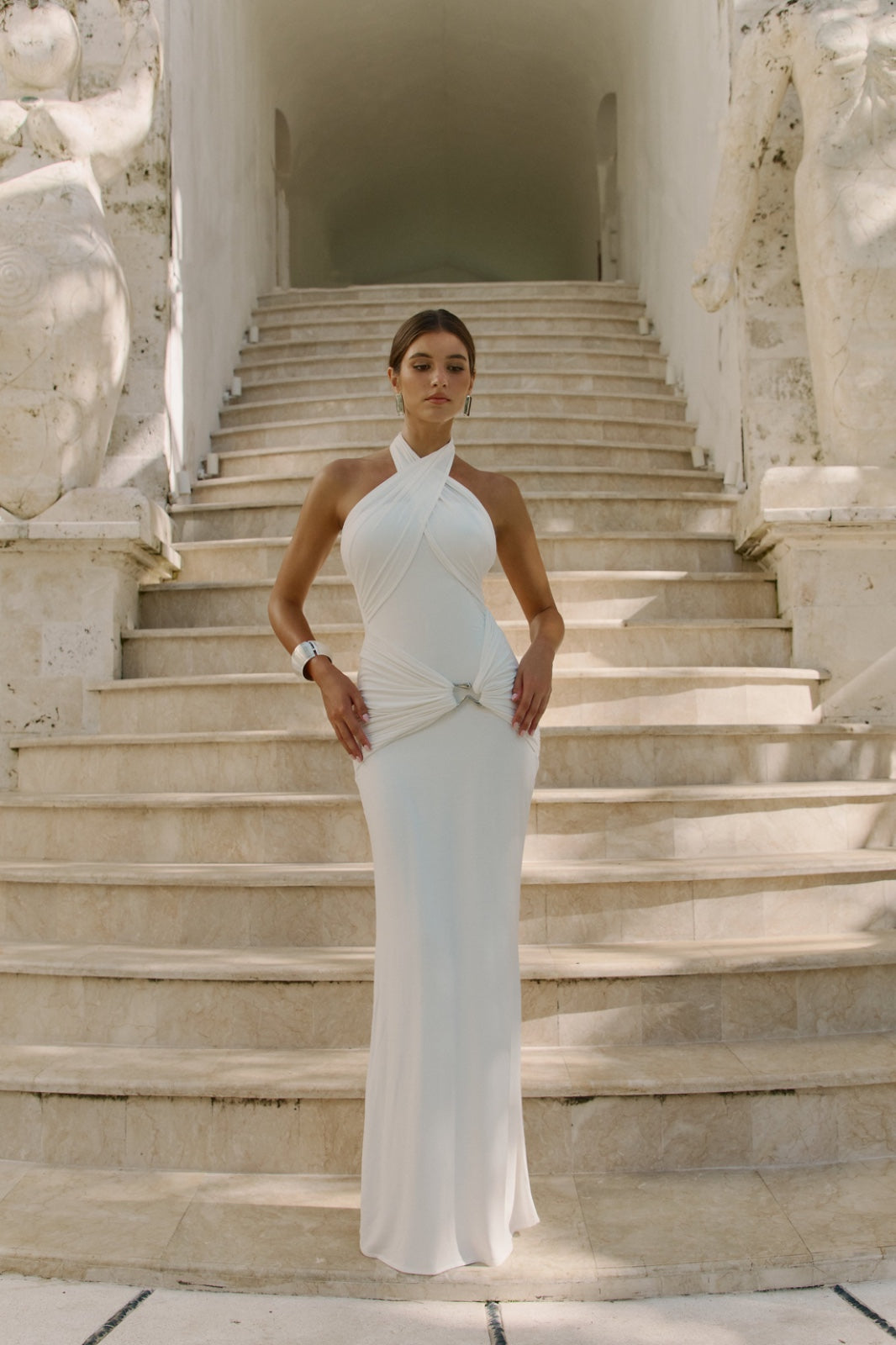 Woman in a white dress standing on stone steps with classical architecture in the background