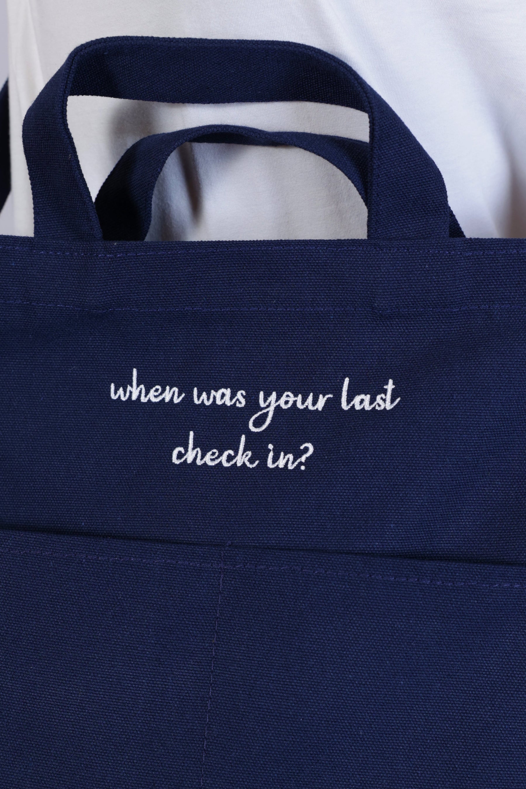Person wearing a navy blue bag "When was your last check in?" - Unisex Tote Bag