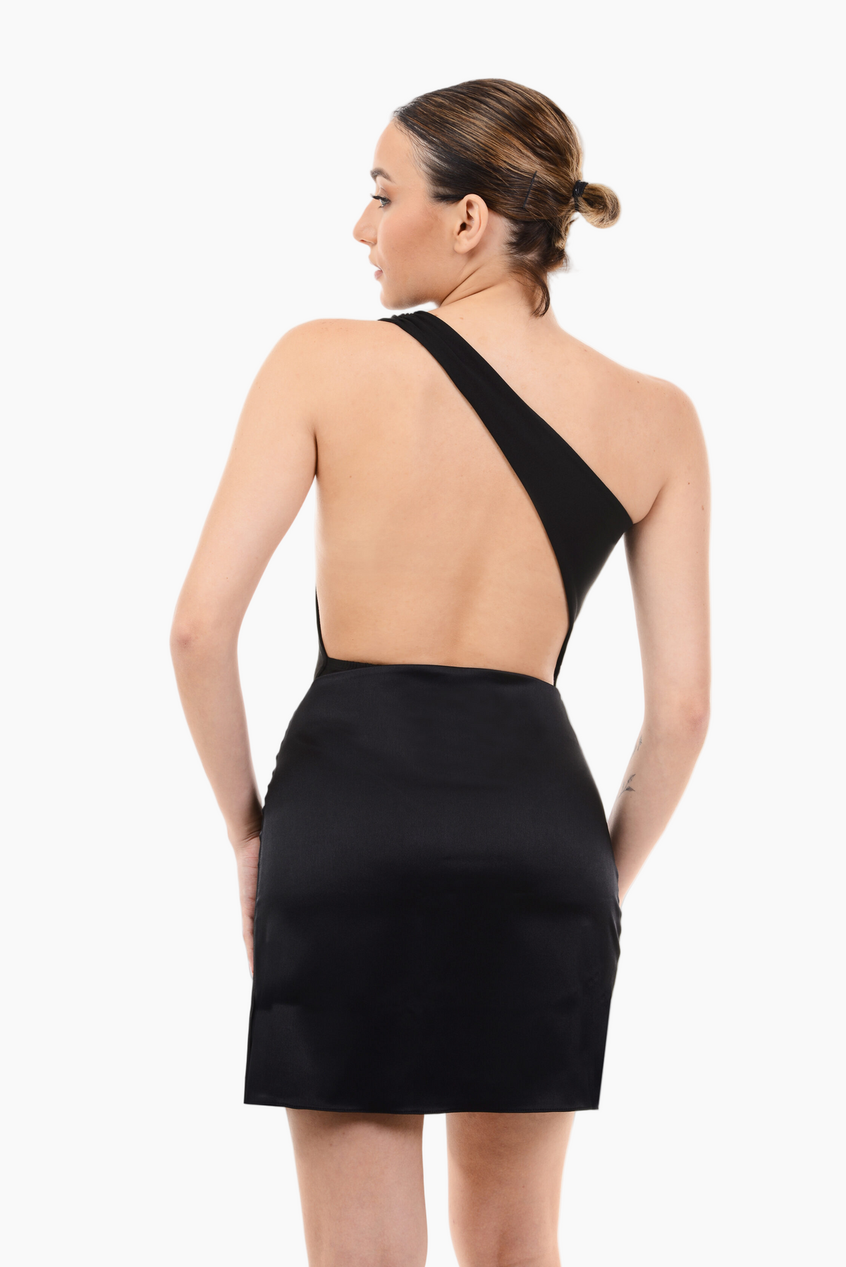 Woman wearing a black one-shoulder bodysuit with an open back on a white background